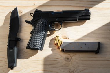 Klasik bir Amerikan tabancası 45 kalibrelik ve güneş ışınlarının altındaki tahta bir yüzeyde taktik bir bıçak..