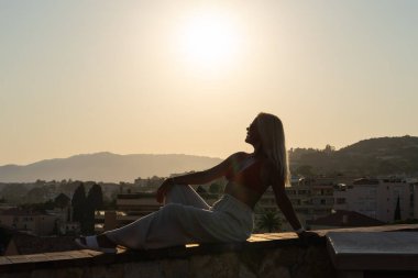 Bir yaz akşamı Cannes şehrinin tepesindeki izleme platformunda oturan bir kadın turist gün batımını izliyor.. 
