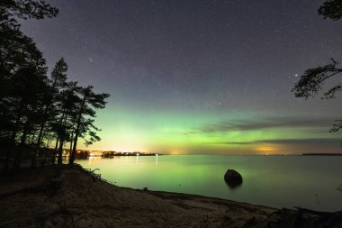 Kaberneeme kıyısındaki sihirli atmosfer: yıldızlı gece gökyüzü, yeşil parıltı ve sakin deniz.