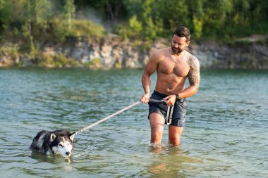 Tasmalı köpekli sportif bir adam açık mavi suyla gölde yüzüyor..