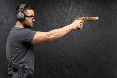 Bir erkek nişancı tek eliyle atış poligonunda tutarken büyük altın renkli bir tabancayı hedef alır.. 