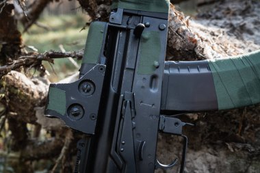 Modifiye edilmiş silahın yakın çekimi: yeşil bant, Picatinny raylarında holografik görüş, detaylı metal dokusu.