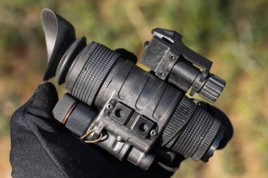 Bulanık bir arka plana karşı eldivenli bir elle modern taktik gece görüşü monoküler yakın plan..