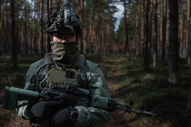 Özel kuvvetler askerleri viteste, miğferinde NVG ve ormanda kırmızı nokta görüşü olan bir tüfek var..