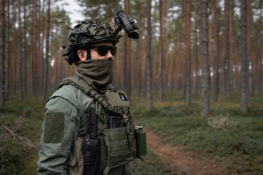 Tam teçhizatlı asker, NVG atlı miğfer, ve güneş gözlüğü, yoğun bir çam ormanında devriye geziyor..