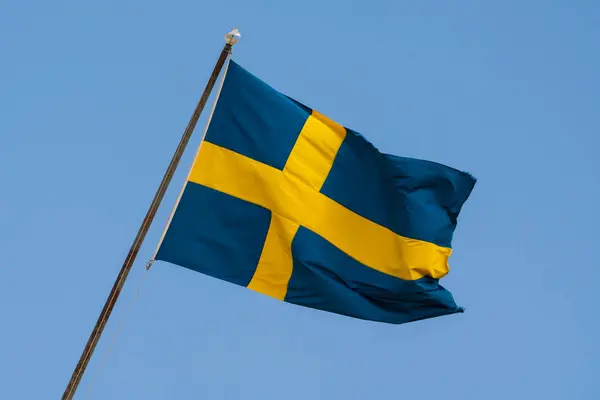 İsveç 'in mavi ve sarı bayrağı açık mavi, güneşli gökyüzüne doğru bayrak direğinde dalgalanıyor..