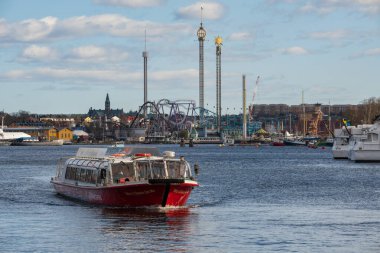 STOCKHOLM, SWEDEN APRIL 4, 2025: Stockholm arka planında Grna Lund lund eğlence parkı olan bir tur teknesi denize açılıyor.