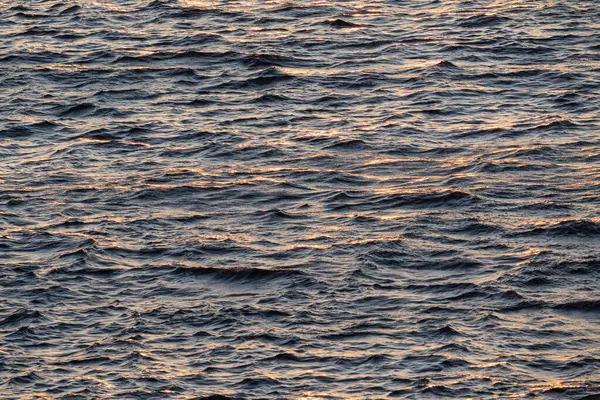 Dalgaların üzerinde altın güneş ışıkları olan koyu su yüzeyinin fotoğrafı; güzel doğal arka plan veya doku.