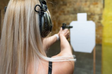 Bir kadın atış poligonunda siluet hedefine ateş ediyor, arka görüş, eğitim konsepti.