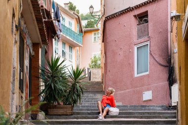 GÜZEL, FRANCE - 29 HAZİRAN 2024: Eski Şehir 'de dar, renkli bir sokakta bir kadın merdivenlerde oturur (Vieux Nice).