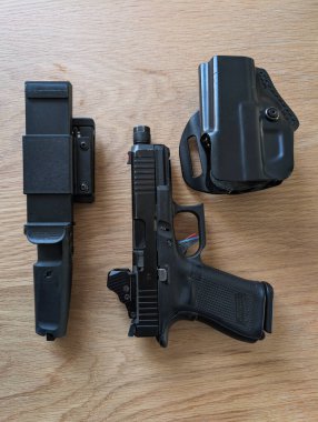 BALTICS - 19 Nisan 2025: Namlusu sivri uçlu Glock 19 tabancası ve kırmızı nokta görüşü, kınında bir Extrema Ratio bıçağı ve bir kılıf.