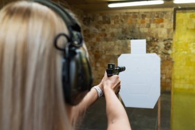 Kapalı alanda atış talimi: Genç bir kadın susturuculu bir tabancaya nişan alıyor ve kulaklık takıyor..