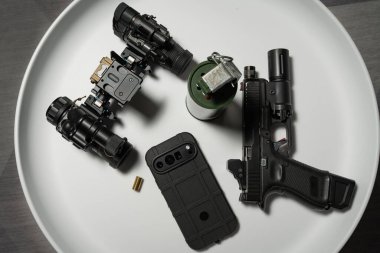 Taktik teçhizat ve modern araçlar: tabanca, el bombası, gece görüşü cihazı, telefon ve boş kovanı beyaz bir masada harcamak..