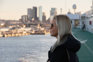 Bir feribotun güvertesindeki genç bir kadın, Baltık Denizi 'ndeki Estonya başkentinden ayrılırken Tallinn siluetinin panoramik görüntüsüne hayran..