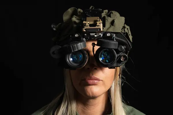 Taktik kasklı ve siyah arka planda gece görüş gözlüklü bir kadının ciddi portresi, gece operasyonlarına ya da gözetlemeye hazır..