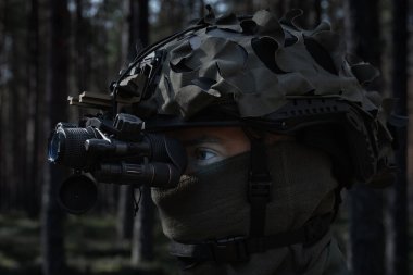 Ormanda gece görüş cihazı (NVD) olan taktik kasklı bir asker.