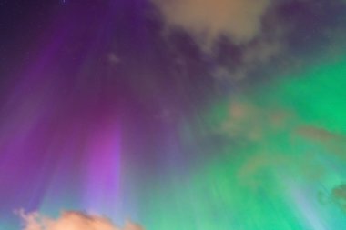 Büyüleyici Kuzey Işıkları gece gökyüzünü bulutların ve yıldızların üzerindeki parlak yeşil ve mor renklerle renklendiriyor..