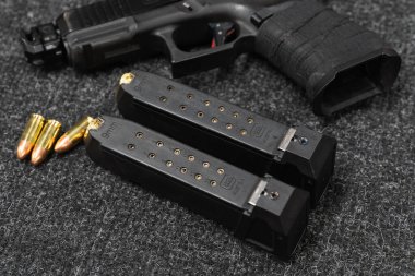The Baltics, 6 Mayıs 2025: Glock 19 mm için iki şarjör, karanlık bir masa üzerindeki tabanca ve mermiler.