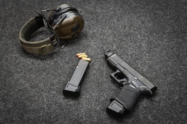 Siyah bir tabanca, dolu bir şarjör ve antrenmandan önce poligonda bir masada taktik kulaklık..