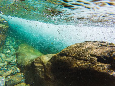 Norveç 'te bir dağ nehrinin kristal berrak suyu: taşların, baloncukların ve güneş ışığı oyununun inanılmaz sualtı manzarası.