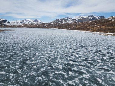 Norveç 'teki Hallingskarvet Ulusal Parkı' nda ilkbahar gökyüzü altında buzların çözülmesiyle büyüleyici donmuş göl..