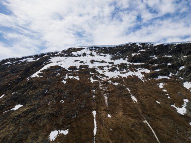 Norveç 'in insansız hava aracına ait dağ manzarası: kahverengi desenli toprak ve kayaları ortaya çıkaran kar kalıntılarıyla dolu bir yay yamacı.
