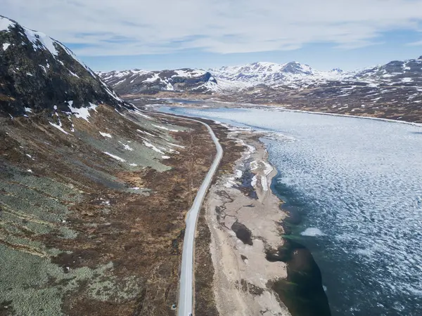 Eldrevatnet Gölü ve karla kaplı zirveleriyle görkemli Norveç dağ manzarasını kesen bir yolun nefes kesici drone görüntüsü..