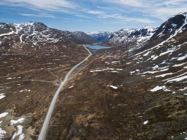 Norveç 'teki görkemli Hemsedal Fjell dağlarından geçen Tindevegen yolunun nefes kesen insansız hava aracı görüntüsü bahar karı kalıntıları ve bir göl. 