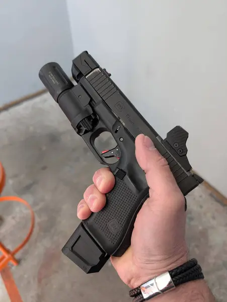 Baltık, 27 Mayıs 2025: Özel yapım bir Glock 19 Gen 5 tabancasının kırmızı nokta görüşlü, silah ışığı ve tetikçinin elinde dengeleyici ile yakın çekimi.