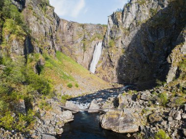 Norveç 'in hava harikası: Voringsfossen şelalesi, engebeli kayalıklar ve zümrüt yeşiliyle çerçevelenmiştir. Vahşi İskandinav doğasının zarif bir manzarası..