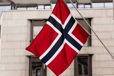 Norveç bayrağı, Norveç Krallığı 'nın ulusal sembolü, modern bir binanın önündeki bayrak direğinde. İskandinav devleti, vatanseverlik ve resmi üç renkli.