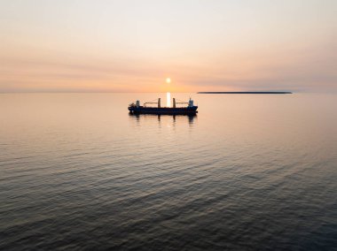 Estonya açıklarında Baltık Denizi: sakin suların ve uzak bir adanın üzerinde sakin bir günbatımına karşı bir kargo gemisi.