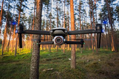 Çam ormanlarında uçan kameralı modern kuadkopter, hareket halindeki pervaneler, doğanın ve ağaçların arka planına karşı havadan görüntü teknolojisi..