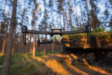 Bir çam ormanının arka planına ve yumuşak günbatımı ışığına yakın çekim kamerasıyla uçan bir dron. Teknoloji ve hava fotoğrafçılığı kavramı.