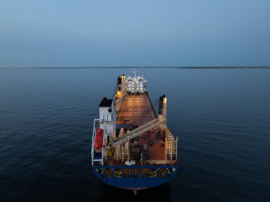 Baltık Denizi 'ndeki kargo gemisi: Alacakaranlık, Estonya' nın kıç manzarası. Geminin aydınlanmış güvertesinin sakin bir denize karşı havadan çekilmiş görüntüsü..