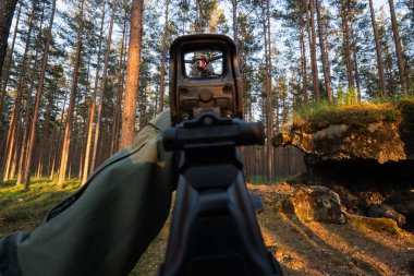 Birinci şahıs görüş: Bir nişancı, orman bölgesinde uçan bir drona holografik görüş açısı olan bir tüfeği hedef alır..