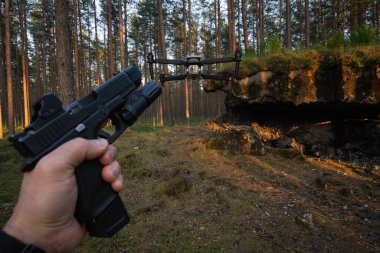 Taktik tabanca elinde, birinci şahıs görüşü: ormandaki eski bir beton sığınağın yakınındaki bir dronu hedef alıyor..