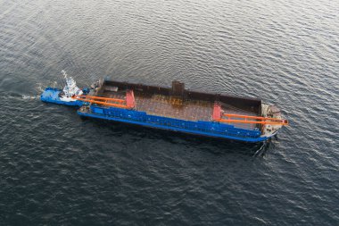 İHA hava aracı: güçlü bir römorkör, deniz operasyonları ve lojistik çalışmaları için su yüzeyinde büyük bir endüstriyel mavna platformunu güvenli bir şekilde çeker.