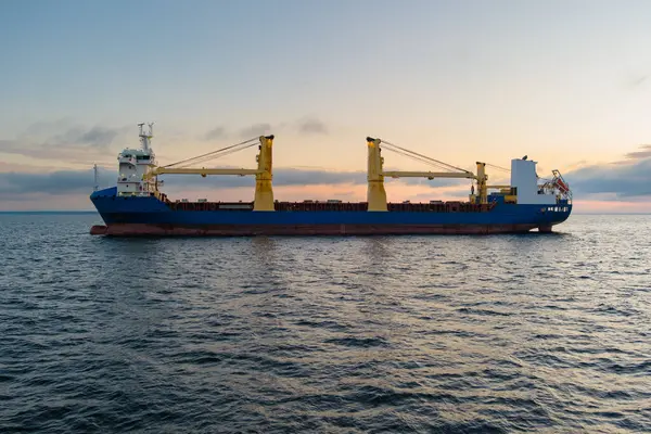 Gün batımında Baltık 'ta mavi gövdeli ve parlak sarı turnalı bir yük gemisi. Bir İHA 'dan havadan çekim. 