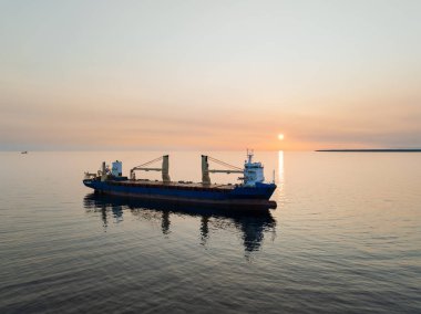 Baltık Denizi sularındaki kargo gemisi, uluslararası ticaret ve lojistiği sembolize eden gün batımına karşı..
