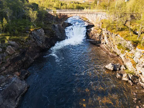 Hava aracı görüntüsü: Güçlü şelale ve Norveç 'te yaz boyunca kayalık bir vadide tarihi taş köprü.