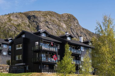 Norveç, Hemsedal - 17 Mayıs 2025: Güneşli bir bahar gününde bir dağ zeminine karşı Norveç bayrağı taşıyan modern Skarsnuten apartmanları.