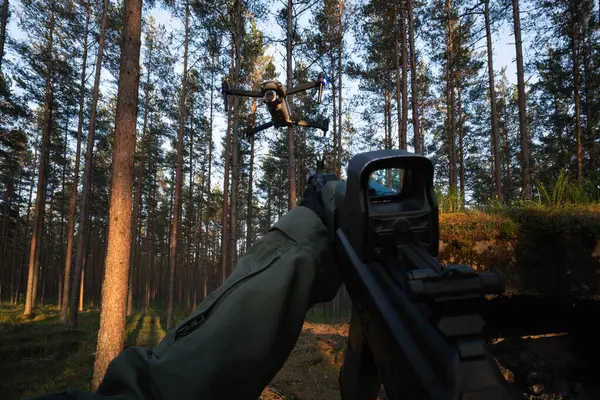 Birinci şahıs bakış açısı: Ormanda uçan bir kuadkopter drone 'a saldırı tüfeği doğrultan asker. Modern savaş ve insansız hava aracı operasyonları kavramı.