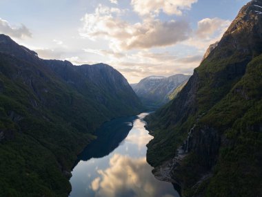 Norveç 'in nefes kesici hava manzarası. İHA 'nın görüntüsü, batan güneşin altın ışıklarındaki yeşil dağların arasına kurulmuş fjord..