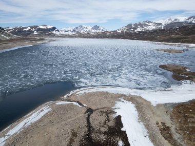 Norveç 'te baharda eriyen buzla kaplı bir dağ gölü manzarası. Sert İskandinav manzarasının insansız hava aracı görüntüsü. Tepelerinde kar var..
