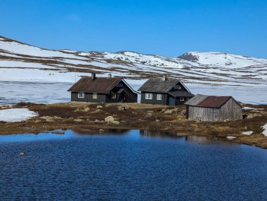 Geleneksel Norveç hitte kulübeleri baharda karlı dağlarda bir gölün kıyısında.