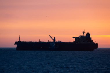 Büyük bir petrol tankeri silueti ve Baltık Denizi 'nde bir ikmal gemisi gün batımından sonra renkli bir gökyüzüne karşı. Deniz taşımacılığı ve küresel ticaret kavramı.