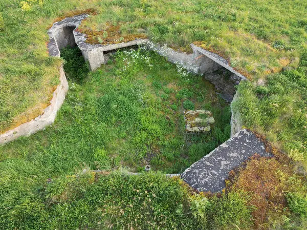 Yeşil çimlerle kaplı terk edilmiş bir Sovyet askeri sığınağının havadan görünüşü. Doğanın tarihi yeniden ele geçirdiği eski bir beton savaş dönemi tahkimatı..