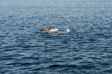 Küçük şişme bir tekne, beyaz bir şamandıraya demirlemiş, engin mavi denizde sakin dalgalarda tek başına sallanıyor..
