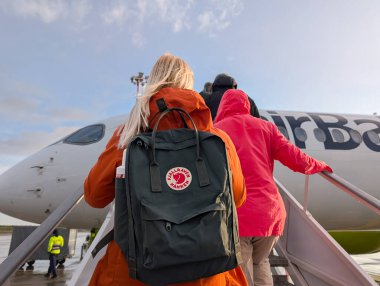 Tallinn, Estonya - 17 Mayıs 2025 Tallinn Havaalanı 'ndan bir AirBaltic uçağına binen yolcular. Fjllrven Knken sırt çantalı bir kadın kalkmadan önce uçağa doğru yürür..